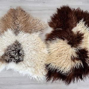Op de afbeelding: Twee schapenvachten met lang, krullend haar. Het linker kleed heeft een mix van crème, beige en donkerbruine vlekken. Het rechter kleed toont een contrastrijk patroon van diepbruine en crèmewitte secties met een ruige textuur.