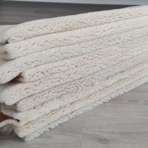 May include: A stack of white sheepskin rugs with brown leather trim. The rugs are soft and fluffy, and they would be perfect for adding a touch of luxury to any room.