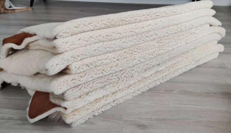 May include: A stack of white sheepskin rugs with brown leather trim. The rugs are soft and fluffy, and they would be perfect for adding a touch of luxury to any room.