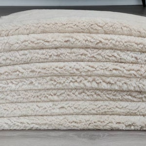 May include: A stack of cream-colored fluffy rugs, likely made of faux fur, with a soft, plush texture.