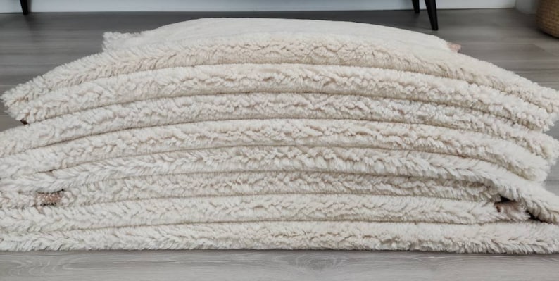 May include: A stack of cream-colored fluffy rugs, likely made of faux fur, with a soft, plush texture.