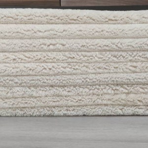 May include: A stack of cream-colored fluffy rugs, likely made of wool or a similar material. The rugs are folded neatly and appear to be new or gently used.