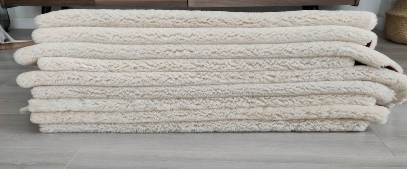 May include: A stack of cream-colored fluffy rugs, likely made of wool or a similar material. The rugs are folded neatly and appear to be new or gently used.