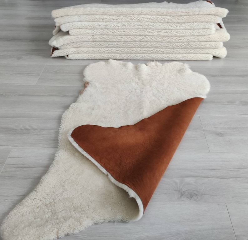 May include: A white sheepskin rug with a brown suede backing. The rug is folded in half, showing both sides.