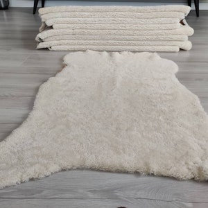 May include: A white sheepskin rug with a fluffy texture. The rug is laid out on a light wood floor.