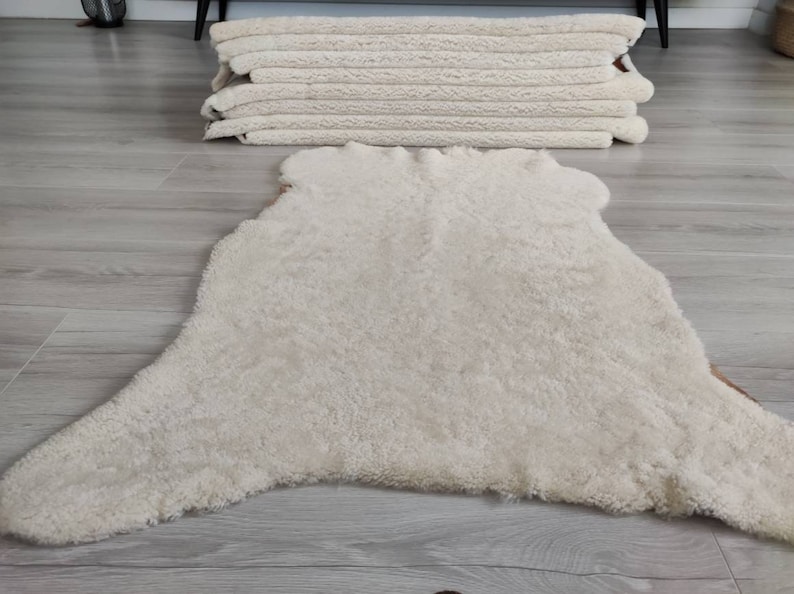 May include: A white sheepskin rug with a fluffy texture. The rug is laid out on a light wood floor.