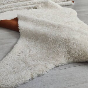 May include: A white fluffy rug with a brown leather border. The rug is shaped like a star and has a soft, plush texture.