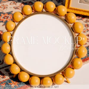May include: A round, white frame with a gold-colored rope-like border, encircled by evenly spaced, spherical, yellow-orange beads. The frame is set against a patterned rug and a white surface. The text "FRAME MOCKUP Photoshop" is visible on the frame.