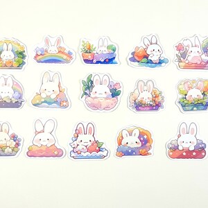 May include: A set of 15 stickers featuring cute white bunnies in various settings. The bunnies are surrounded by flowers, rainbows, and other whimsical elements. The stickers are perfect for adding a touch of whimsy to journals, laptops, or other surfaces.