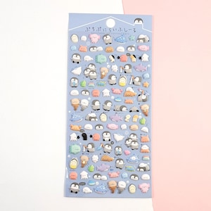 Puede incluir: Una hoja de pegatinas hinchadas de colores con ping&uuml;inos, ballenas, peces y otras criaturas marinas. Las pegatinas est&aacute;n sobre un fondo azul y tienen el texto japon&eacute;s "ぷちぷにぷちシール" que se traduce como "Puchi Puchi Seal".