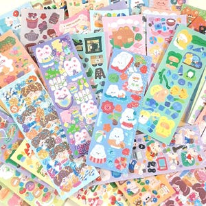 May include: A selection of vibrant sticker sheets with charming illustrations. Designs include cartoon characters, food items, and decorative elements in shades of blue, pink, green, and purple. These stickers are suitable for scrapbooking and crafts.
