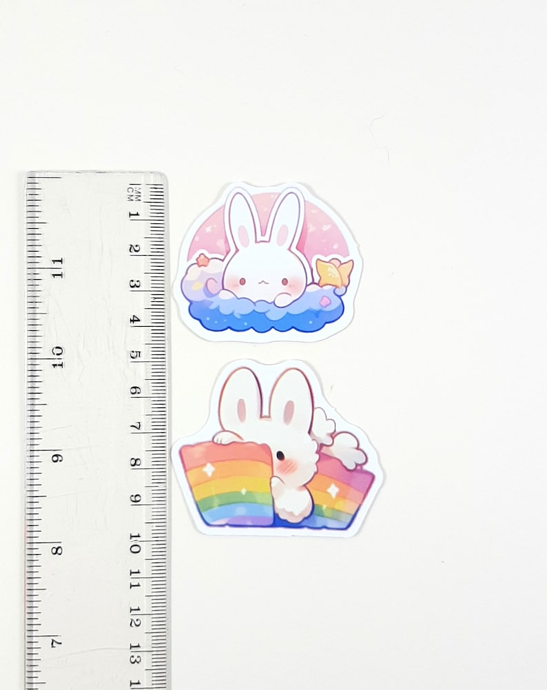 May include: Two stickers featuring a white bunny rabbit. The first sticker shows the bunny in a blue cloud with pink stars and a yellow star. The second sticker shows the bunny holding a rainbow.