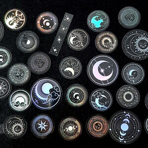 Könnte beinhalten: Eine Sammlung von Aufklebern zum Thema Himmel mit Monden, Sonnen, Sternen und Wolken in verschiedenen Designs. Die Aufkleber haben ein holografisches, irisierendes Finish mit silbernen und pastellfarbenen Akzenten. Die Aufkleber sind rund.