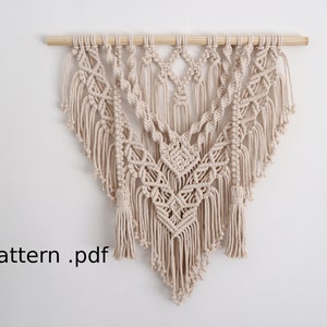 May include: A beige macrame wall hanging with detailed woven designs and tassels. The textile art is suspended from a natural wooden dowel. The text "Pattern .pdf" is visible in the lower left corner.