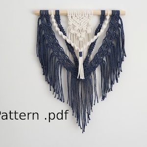 May include: A white and navy blue macrame wall hanging with a wooden dowel at the top. The macrame is in a triangular shape with fringe at the bottom. The text "Pattern.pdf" is visible at the bottom left of the image.