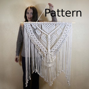 以下が含まれることがあります： 幾何学模様とフリンジが付いた白いマクラメの壁掛け。高さは約120cm、幅は約90cm。壁掛けの上には黒い文字で「Pattern」と書かれている。