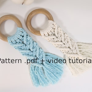 May include: Two macrame baby teethers with wooden rings. One teether is blue and white, the other is white. The image includes the text "Pattern .pdf + video tutorial".