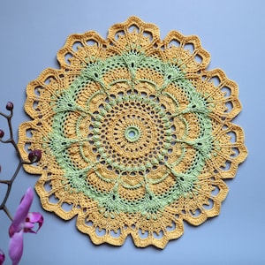 May include: A crocheted doily with a yellow and green color scheme. The doily has a circular shape and a delicate, intricate design.