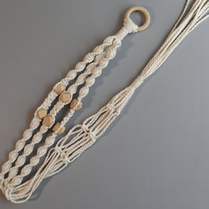 May include: A macrame plant hanger with a wooden ring at the top and wooden beads woven into the design. The hanger is made of natural cotton cord and is a light beige color.