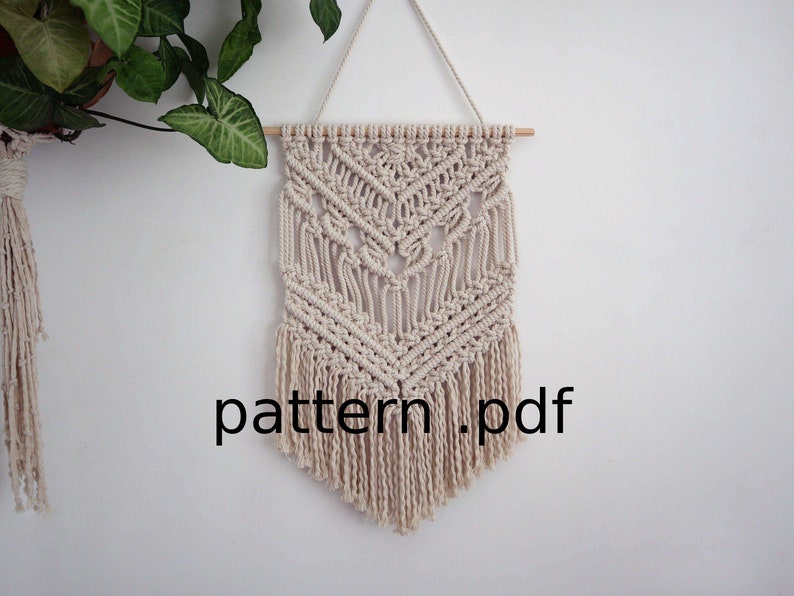 May include: A beige macrame wall hanging with a geometric pattern and fringe. The hanging is attached to a wooden dowel rod. The text "pattern.pdf" is visible at the bottom of the image.