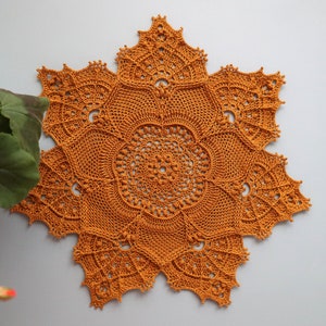 Op de afbeelding: Een groot, gehaakt tafellaken in een warme, mosterdgele kleur. Het tafellaken heeft een stervorm met ingewikkelde details en een delicate, kant-achtige textuur.
