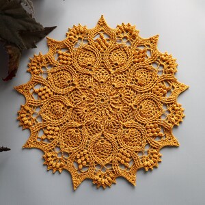 Puede incluir: Un encaje de ganchillo amarillo con un diseño circular y un patrón de estrella alrededor del borde.