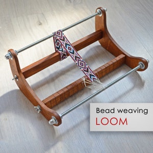 Peut inclure: Un métier à tisser en bois pour perles avec un projet de perles en cours. Le métier à tisser a deux tiges métalliques et une base en bois. Le texte "Bead weaving LOOM" est visible sur l'image.
