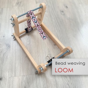May include: A wooden bead weaving loom with a beaded project in progress. The loom has a wooden frame with adjustable tension knobs and a metal rod for holding the beads. The project is a colorful beaded band with a geometric pattern.