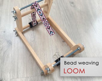 May include: A wooden bead weaving loom with a beaded project in progress. The loom has a wooden frame with adjustable tension knobs and a metal rod for holding the beads. The project is a colorful beaded band with a geometric pattern.