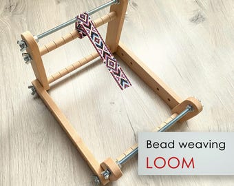 May include: A wooden bead weaving loom with a partially woven beaded strip. The strip features a geometric pattern in shades of red, black, and white. The text "Bead weaving LOOM" is displayed on a white rectangle.