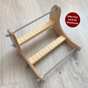 May include: A wooden bead loom with a natural finish. The loom features two parallel wooden bars with evenly spaced grooves, connected by wooden side pieces and metal rods. Wing nuts and bolts secure the structure. The loom is designed for crafting.
