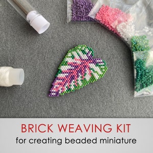 Op de afbeelding: Brick weaving kit voor het maken van een miniatuur blad van kralen. De kit bevat groene, witte, roze en paarse kralen, draad en een naald.