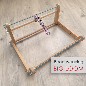 May include: A wooden bead weaving loom with a woven beaded strip. The loom has a rectangular frame with horizontal dowels and metal rods. The text "Bead weaving BIG LOOM" is in a white box.