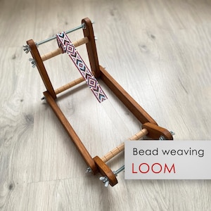 Pode incluir: Um tear de madeira para tecer contas com uma tira de contas coloridas anexada. O tear é feito de madeira marrom e tem um fio branco passando por ele. O texto "Bead weaving LOOM" está impresso no canto inferior direito da imagem.
