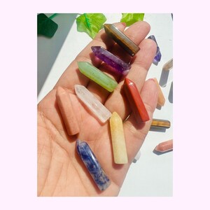 May include: A collection of small, polished crystal points in various colours including brown, purple, green, clear, red, yellow, and blue-white. These smooth, hexagonal-shaped stones are arranged in a cluster, showcasing distinct natural hues and textures.