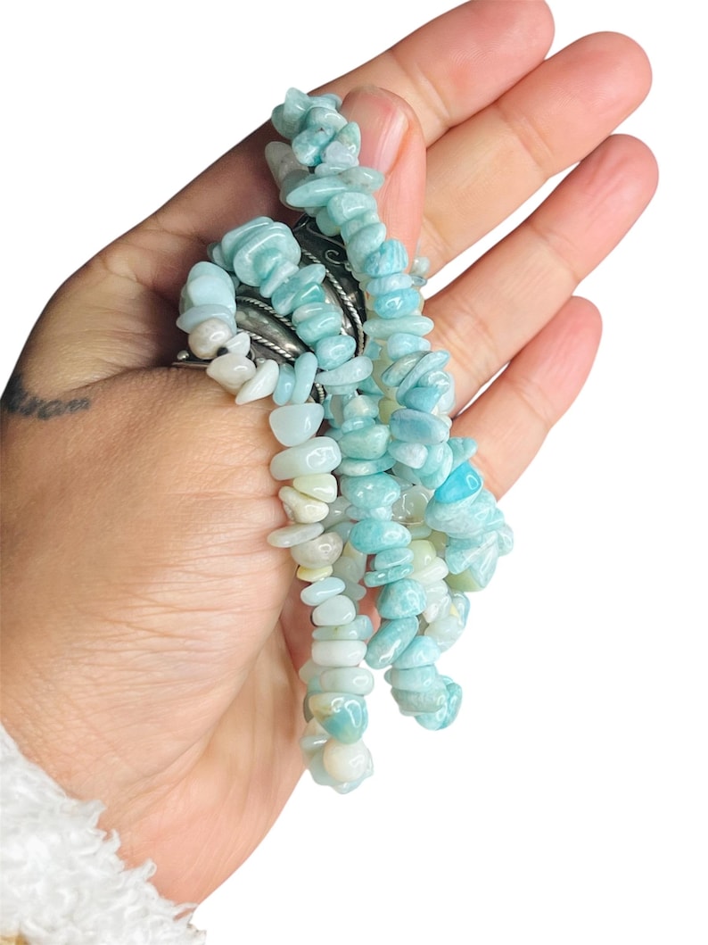 May include: A bracelet composed of multiple strands of tumbled, light blue and white stone chips. The stones have a smooth, polished texture and vary in size and shape, creating a layered appearance. The bracelet is secured with a silver-toned metal clasp.