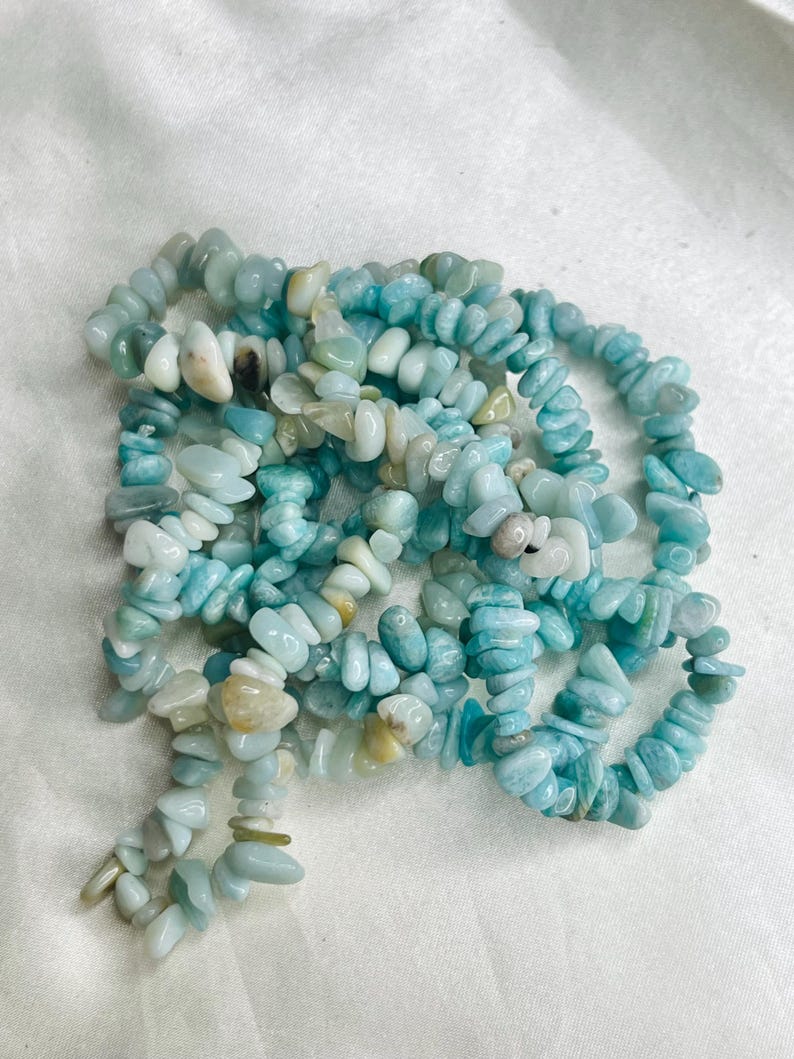 May include: A strand of tumbled, irregular chip beads in shades of light blue, turquoise, and pale green. The polished stones are strung together, creating a textured, multi-layered appearance with variations in opacity and color saturation.