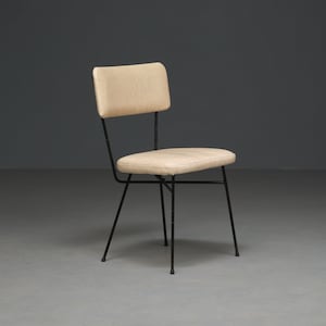 Może przedstawiać: Krzesło w stylu retro z kremowym siedziskiem i oparciem. Krzesło ma czarną metalową ramę z czterema nogami i minimalistyczny design. Siedzisko i oparcie są tapicerowane.