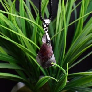 May include: A purple and grey crystal pendant on a black cord. The pendant is faceted and has a silver bail.