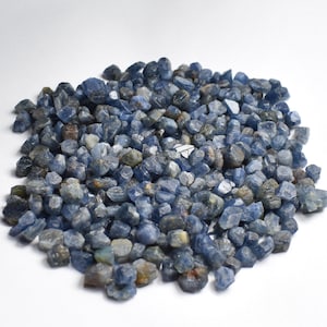 May include: A large pile of rough, blue sapphire gemstones. The sapphires are various sizes and shapes, with a deep blue colour.