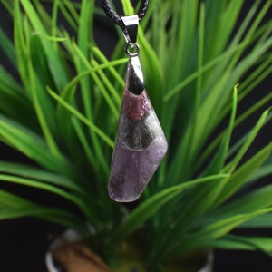May include: A silver pendant featuring a purple, black and pink amethyst stone. The pendant is suspended from a black cord.