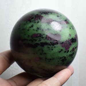 May include: A green, black, and purple gemstone sphere. The sphere is smooth and polished.