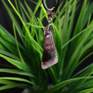 May include: A silver pendant featuring a triangular amethyst gemstone. The gemstone has a layered pattern of purple, black and white.