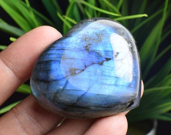 May include: A heart-shaped blue labradorite crystal with iridescent shimmer. The crystal is smooth and polished, with a dark blue color and flashes of green and gold.
