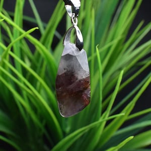 May include: A purple and grey crystal pendant with a silver bail. The crystal is a natural stone with a unique pattern and is set in a silver pendant.
