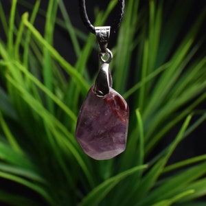 May include: A purple amethyst pendant with a silver bail, hanging from a black cord. The pendant is a freeform shape and has a natural, rough texture.