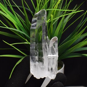 Könnte beinhalten: Ein Cluster aus drei klaren Quarzkristallen mit einer spitzen Form. Die Kristalle sind in einem vertikalen Stapel angeordnet, wobei der größte Kristall unten und der kleinste oben liegt.