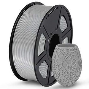 Pu&ograve; includere: Un rotolo di filamento color argento per la stampa 3D. Il filamento &egrave; avvolto attorno a un rotolo di plastica nera con un foro centrale. Il rotolo &egrave; su una superficie bianca.