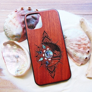 May include: A red wooden phone case with a black mandala design and a moon and wolf illustration. The design features a mother of pearl inlay in the centre of the moon.