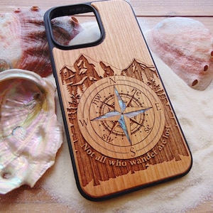 May include: A wooden phone case with a compass design and the text "Not all who wander are lost". The compass features a star with a mother-of-pearl center.